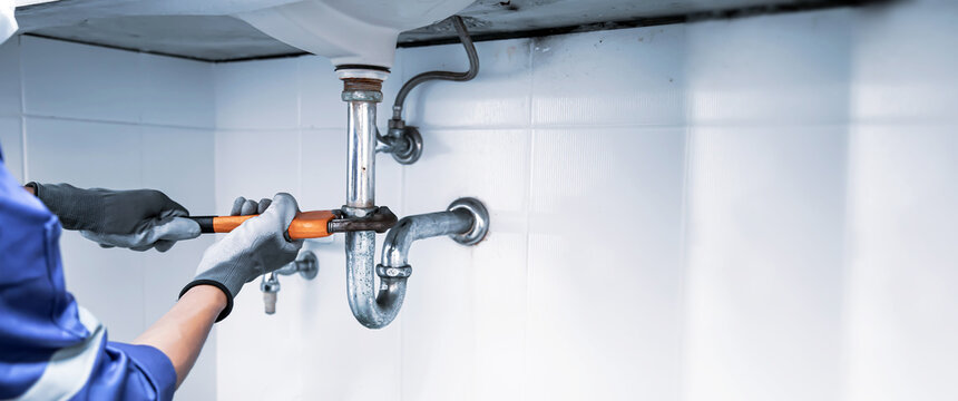 A man doing some plumbing work under a sink.